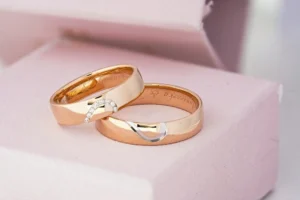 Pair of custom gold wedding bands with diamond details, elegantly placed in a soft pink cushion-lined box.