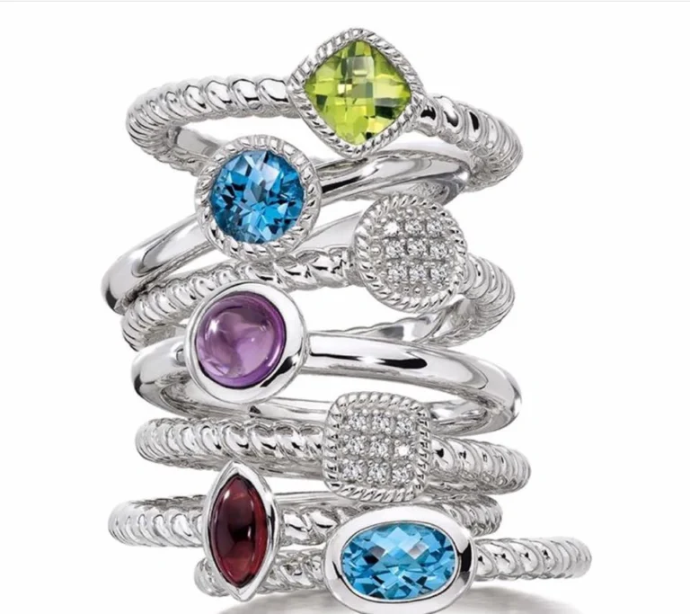 Close-up of sterling silver rings stacked on top of one another, featuring green, blue, purple, white, dark red, and light blue gemstones.