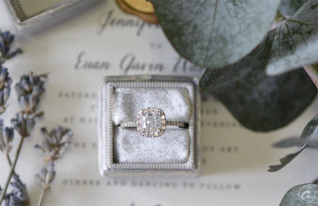 A radiant diamond engagement ring, with alternating round and marquise diamonds on the band, placed atop a rose.
