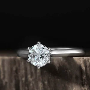 A round brilliant cut diamond set in a 6 prong knife edge platinum ring, resting on a wooden surface.