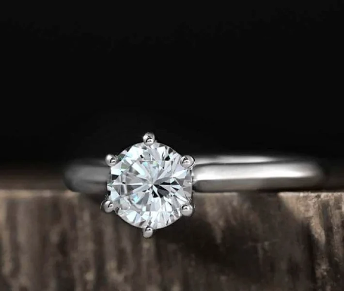 A round brilliant cut diamond set in a 6 prong knife edge platinum ring, resting on a wooden surface.