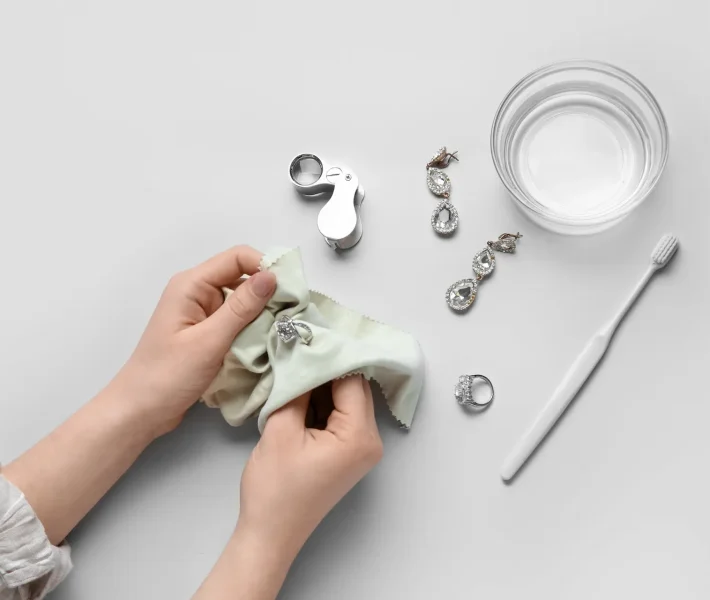 Woman polishing beautiful ring with napkin on white background