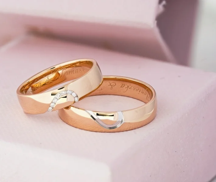 Pair of custom gold wedding bands with diamond details, elegantly placed in a soft pink cushion-lined box.